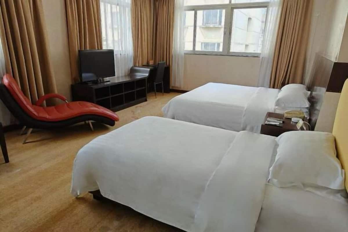 A hotel room with two beds, a TV, a desk, and a red chair.