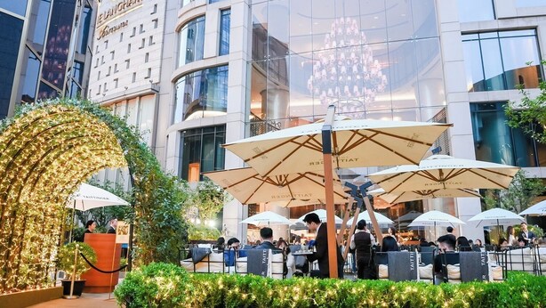 Un área de comedor al aire libre con varias sombrillas, una recepción y un edificio moderno al fondo.