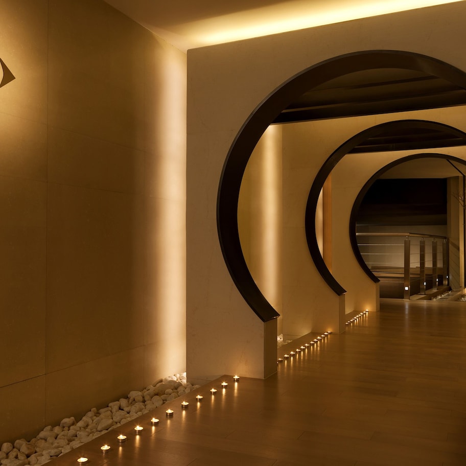 A hallway with a circular archway, a spa sign, and a row of candles on the floor.
