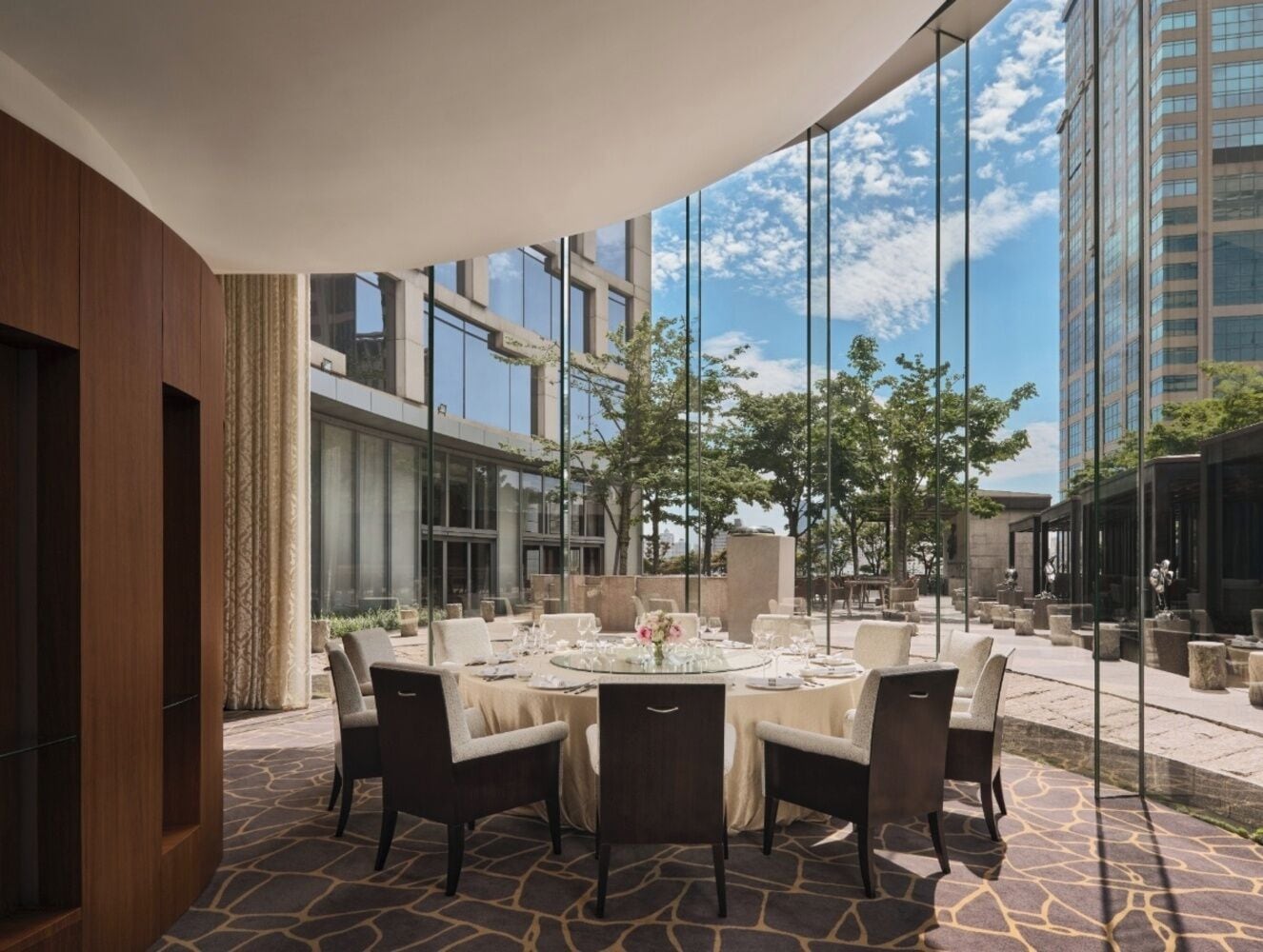 An outdoor dining area with a round table, chairs, and a view of a modern building and trees.