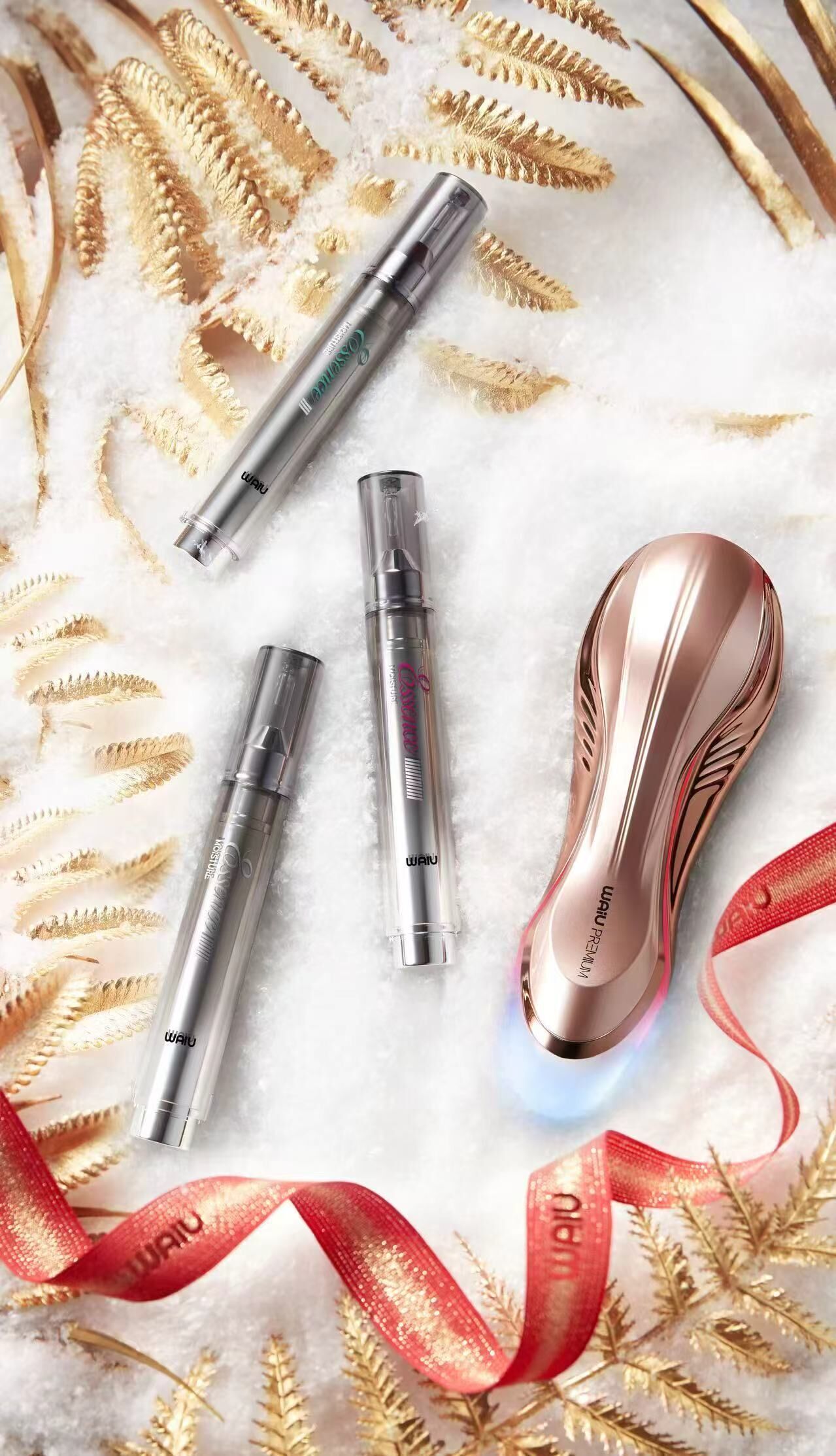 A collection of cosmetic products on a white surface with decorative golden fern leaves and a red ribbon.