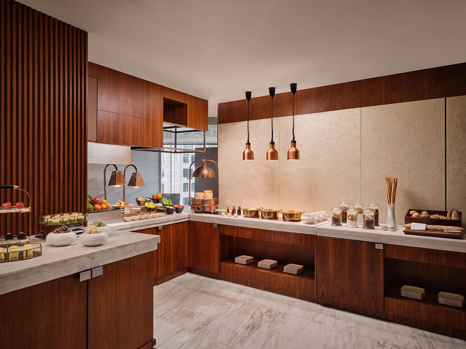 A modern kitchen with wooden cabinets, marble countertops, and copper pendant lights.