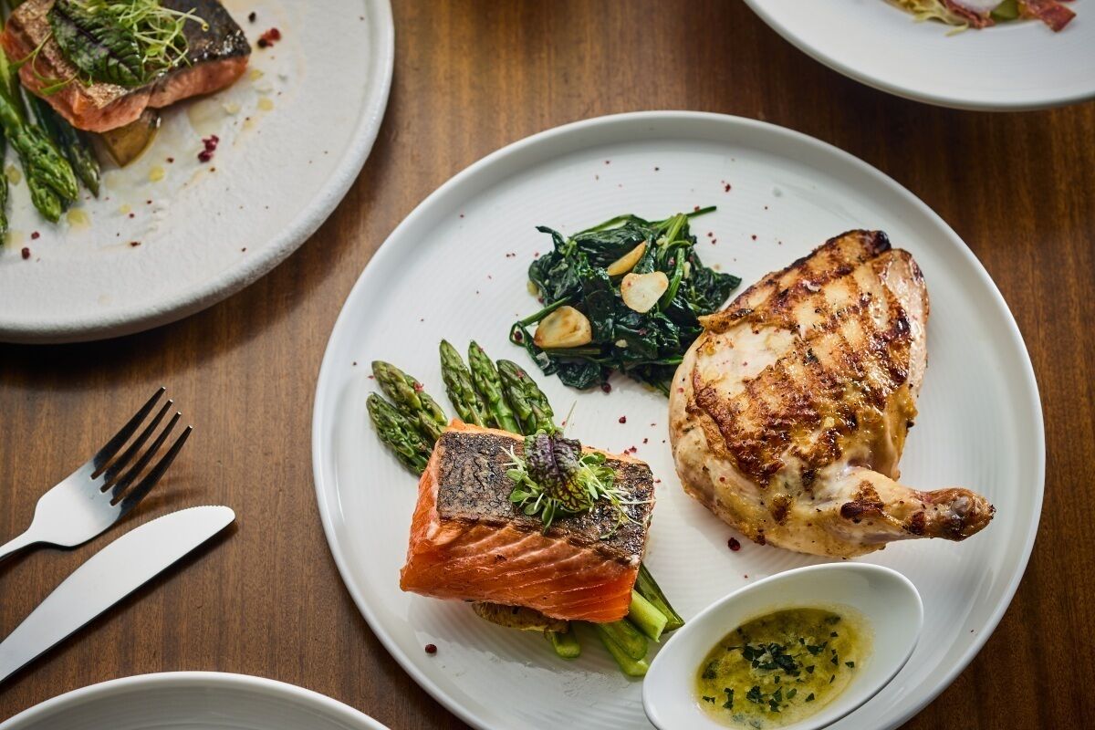 A dining table with plates of food, including salmon and chicken, asparagus, and a small bowl of sauce.