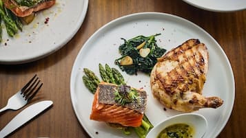 A dining table with plates of food, including salmon and chicken, asparagus, and a small bowl of sauce.