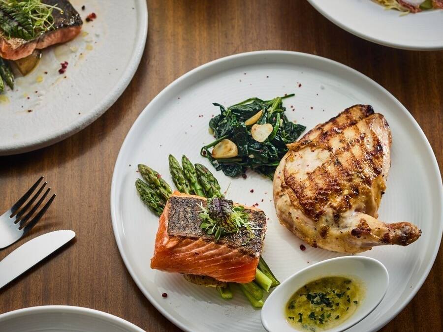 A dining table with plates of food, including salmon and chicken, asparagus, and a small bowl of sauce.