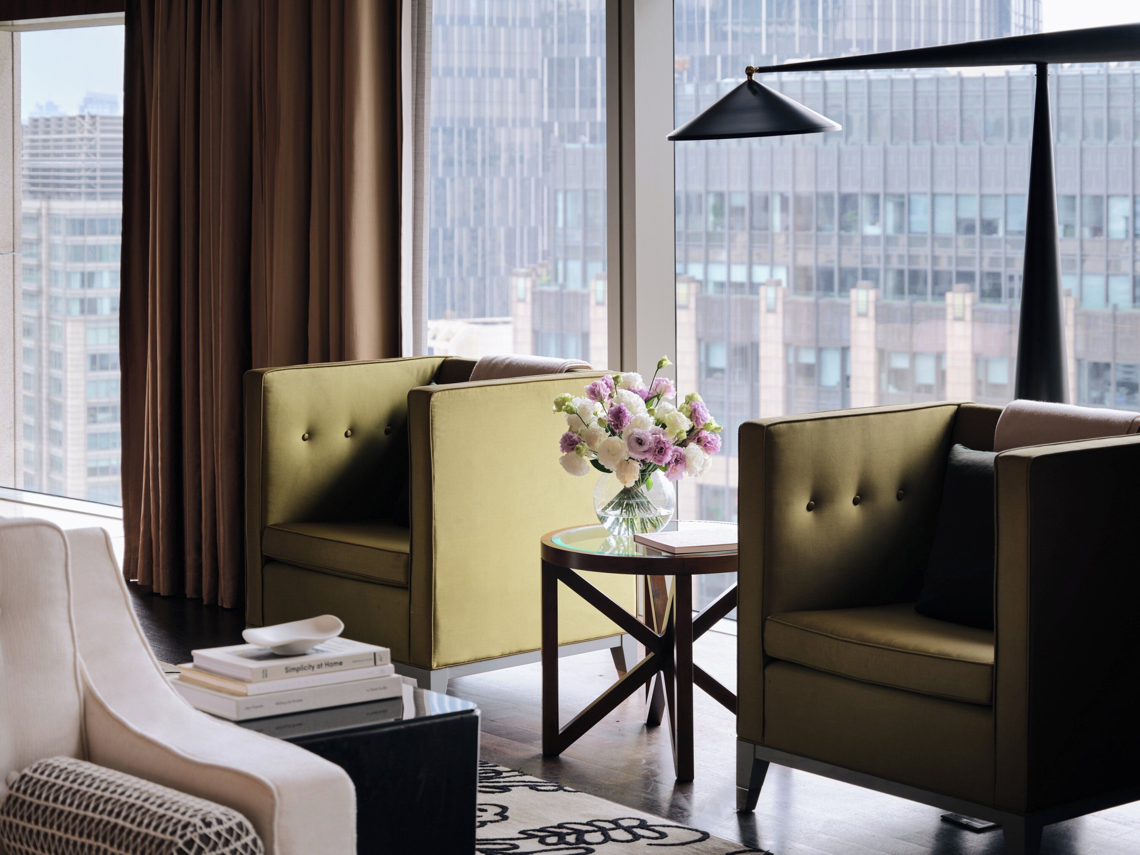 A modern hotel room with a sofa, armchair, and a small table with a vase of flowers.