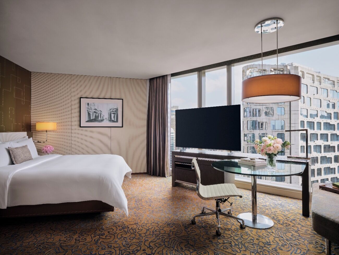 Habitación de hotel con cama, escritorio, silla, televisión y ventana grande con vista a la ciudad.