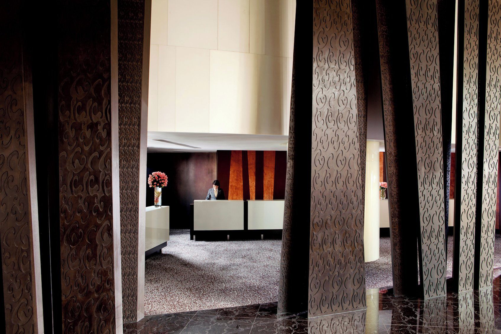 A reception area with a receptionist desk, patterned columns, and a carpeted floor.