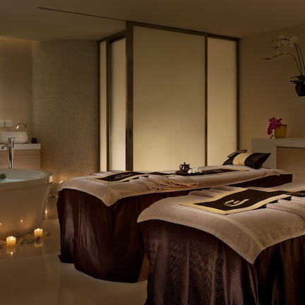A spa room with a bathtub, two massage tables, candles, and a mirror.
