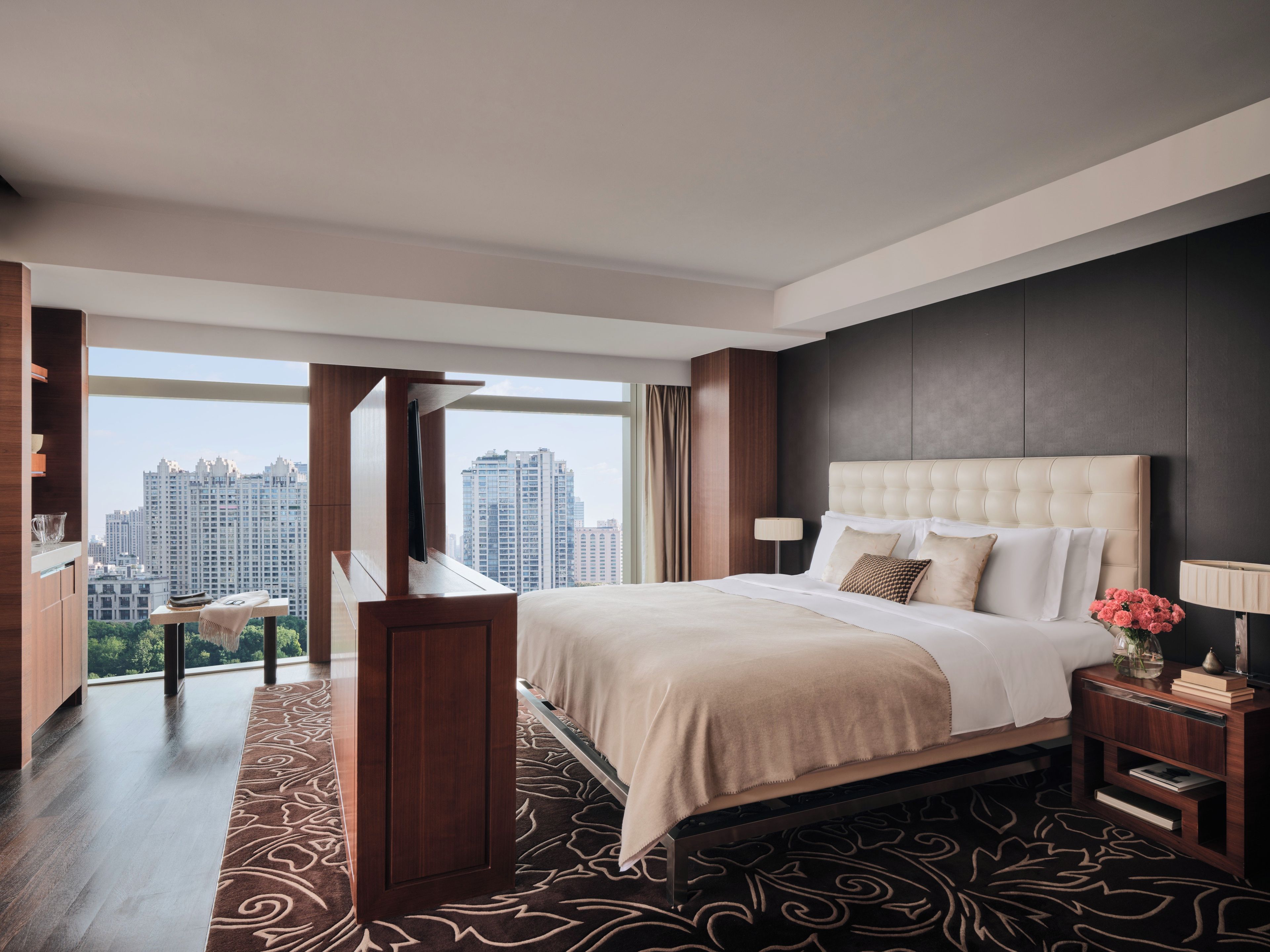 A modern hotel room with a large bed, a view of the city, and a wooden floor.