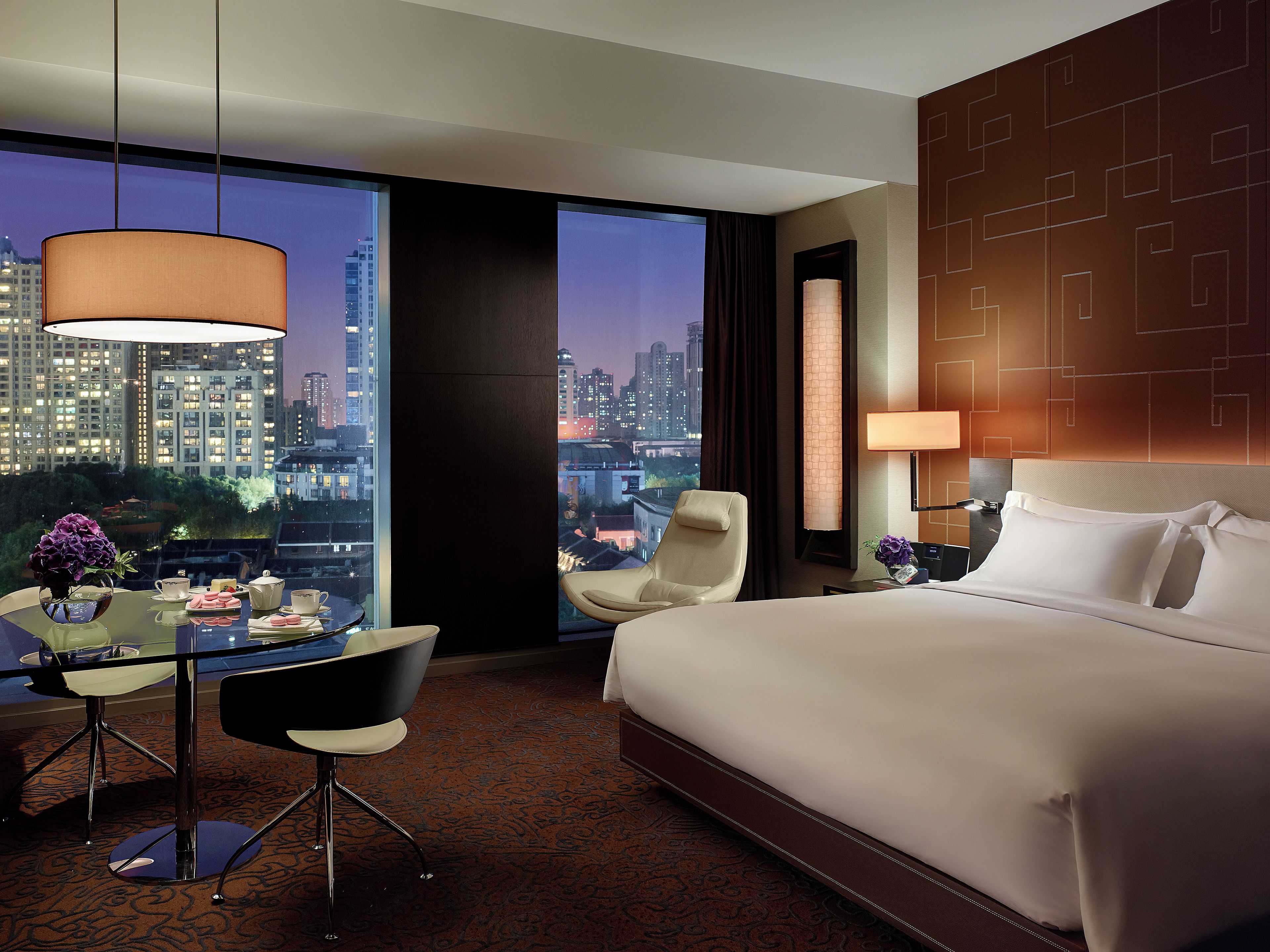 Una camera d'albergo con un letto grande, una scrivania con una sedia, vista sulla città e sullo skyline urbano visibile dalla finestra.