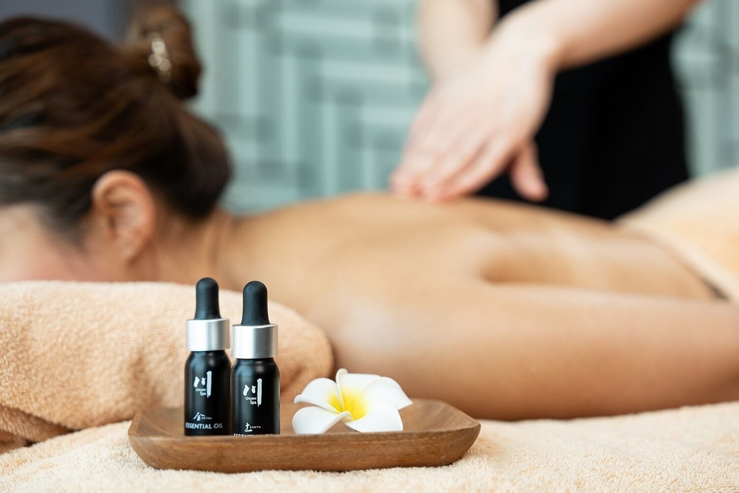 A massage session with essential oil bottles and a flower on a tray.