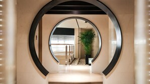 Un pasillo moderno con un espejo circular, una planta en maceta y una barandilla de madera.