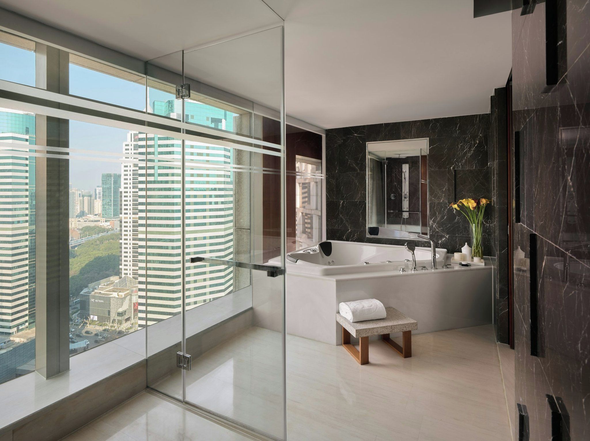 A modern bathroom with a large bathtub, a glass-enclosed shower, and a city view.