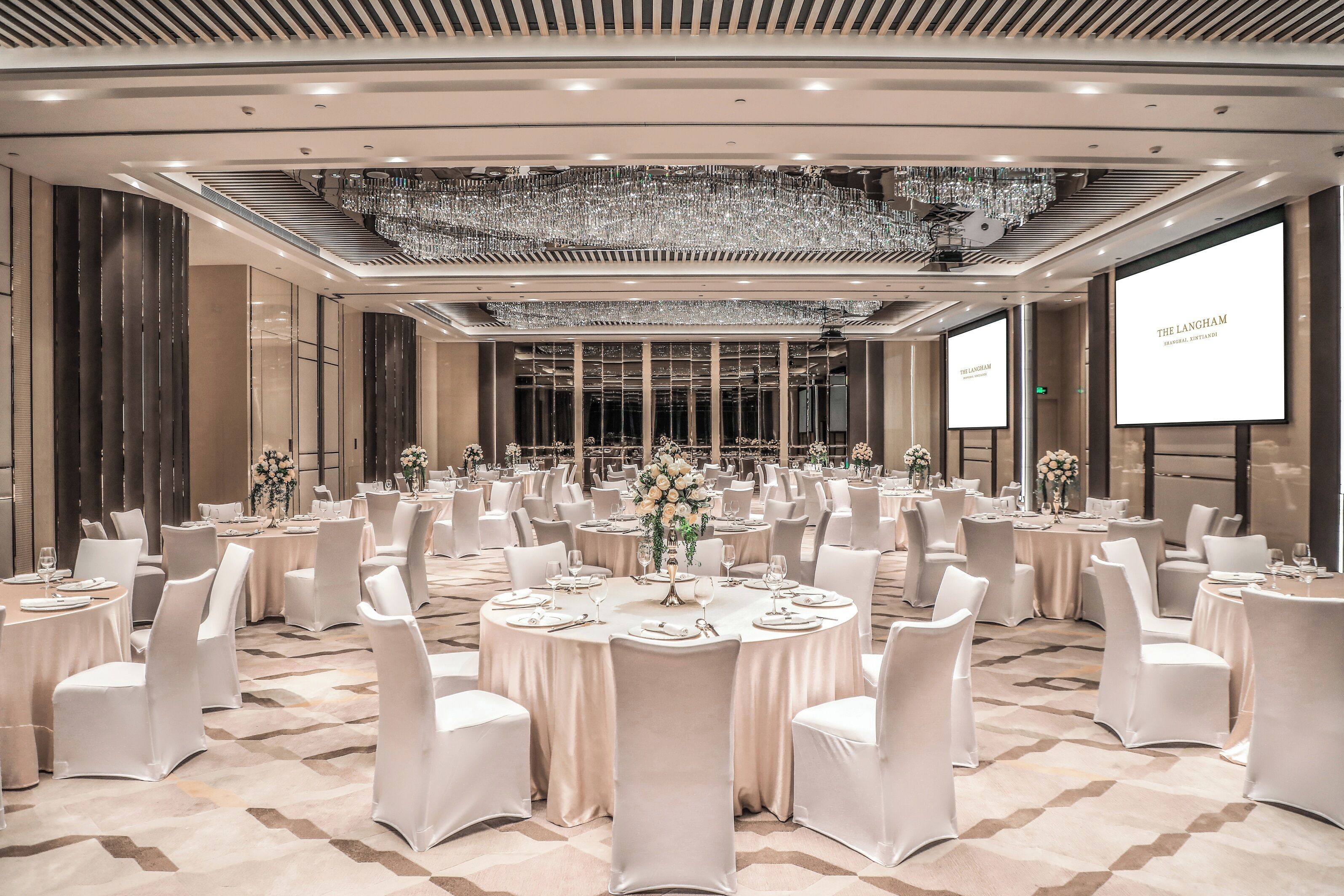 A banquet hall with round tables, white chairs, chandeliers, and a large screen displaying 'THE LANGLEHAM.'