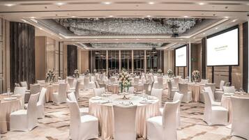 A banquet hall with round tables, white chairs, chandeliers, and a large screen displaying 'THE LANGLEHAM.'