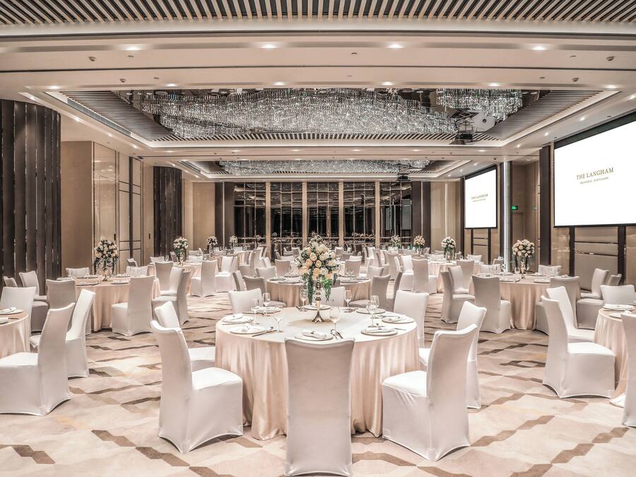 A banquet hall with round tables, white chairs, chandeliers, and a large screen displaying 'THE LANGLEHAM.'