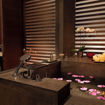 A modern bathroom with a large mirror, a sink with a chrome faucet, and a small window with horizontal blinds.