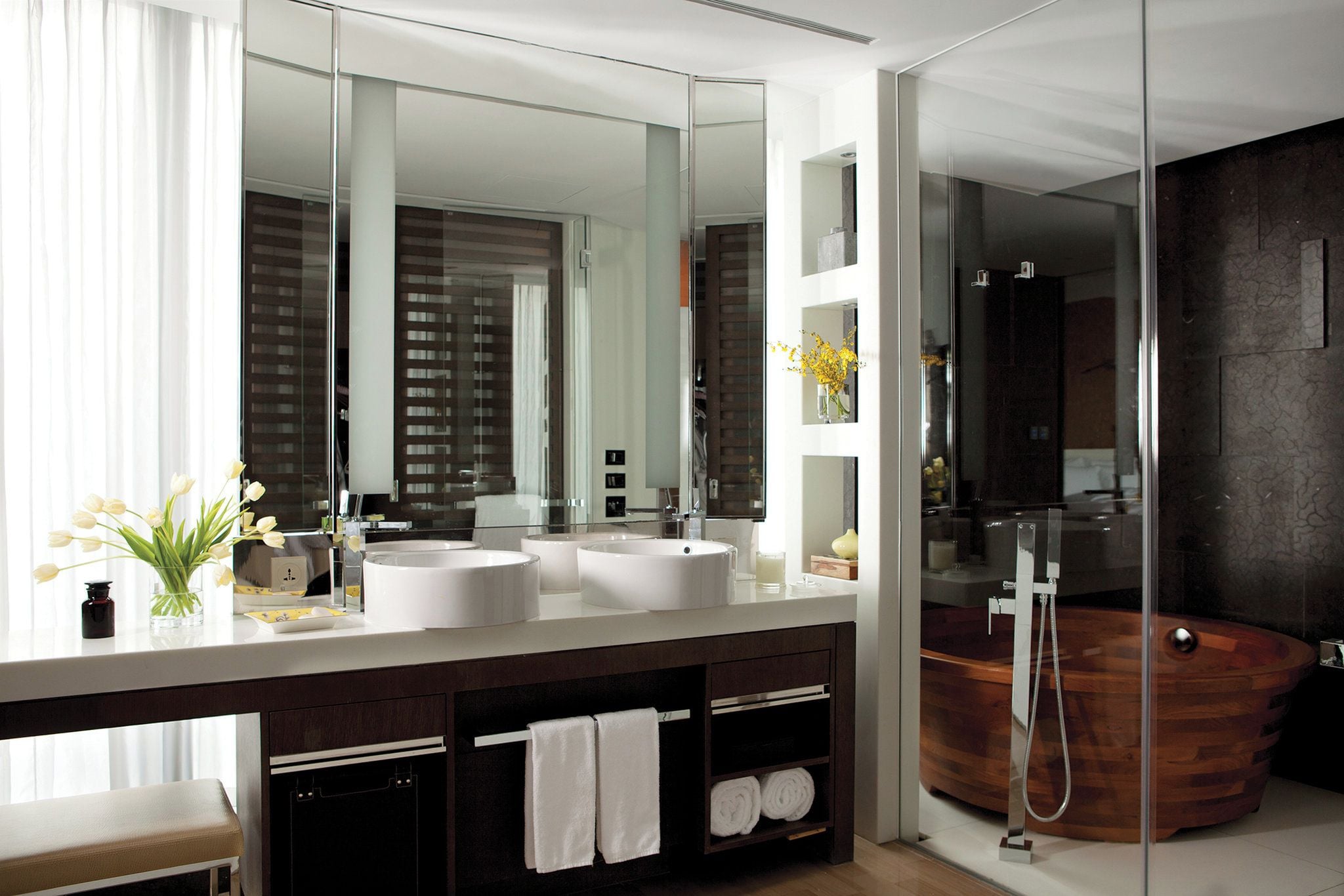 A modern bathroom with a large mirror, two sinks, a bathtub, and a shower.