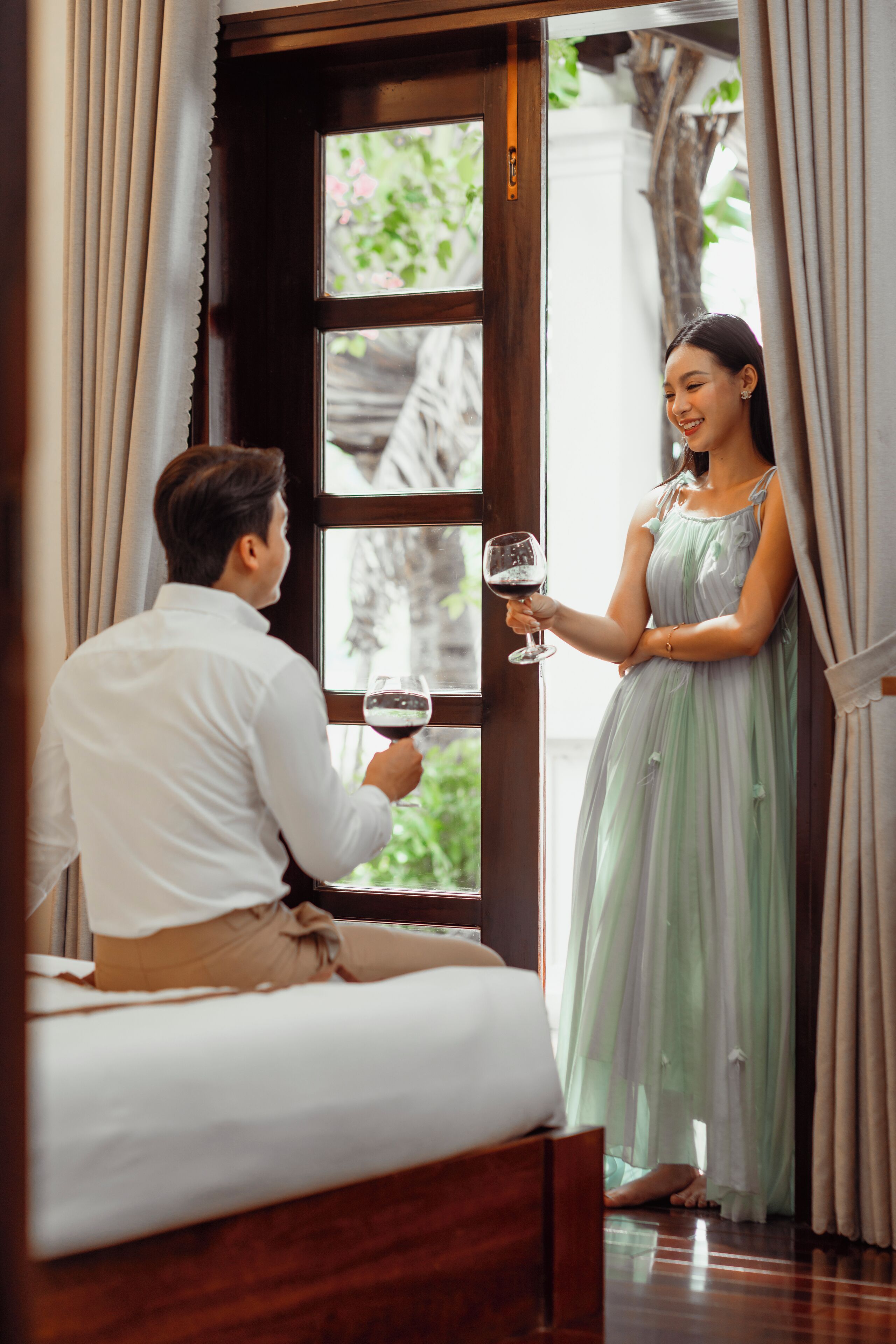 A man and woman in a room with a bed, a window, and curtains.
