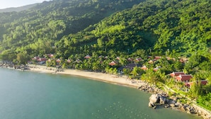 A coastal resort with beach huts, palm trees, and a mountainous backdrop. - Son Tra Resort (Da Nang)