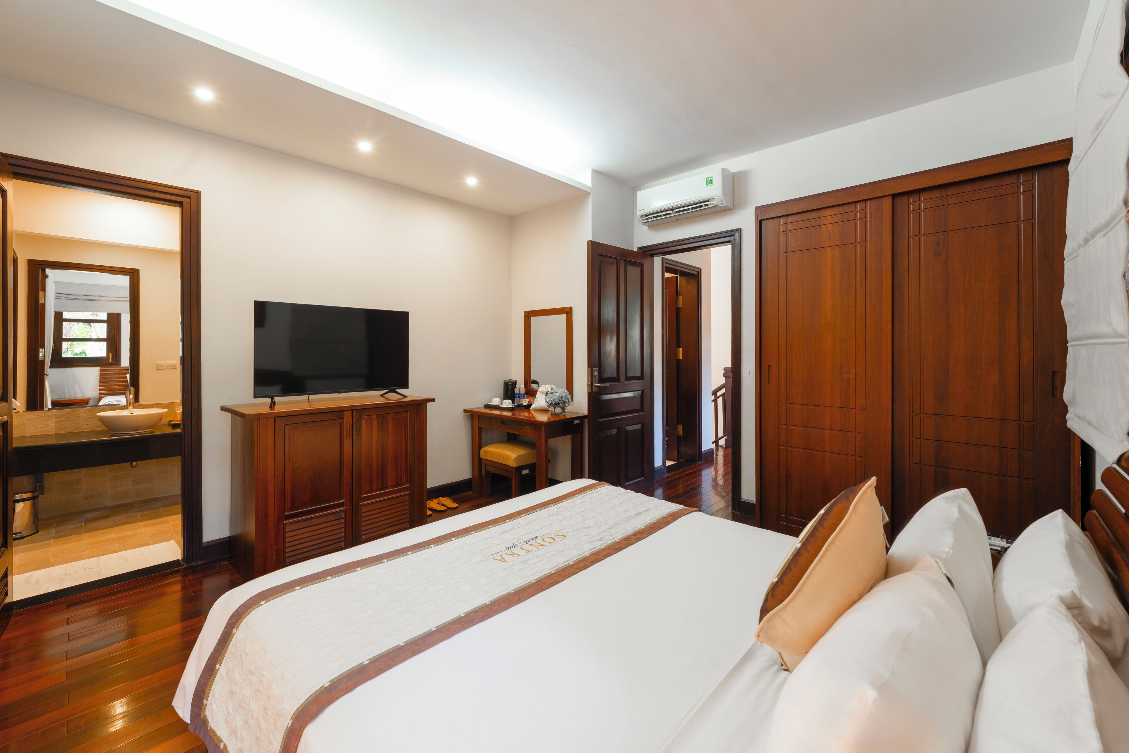 A hotel room with a large bed, a television, a desk, a chair, and a wardrobe.