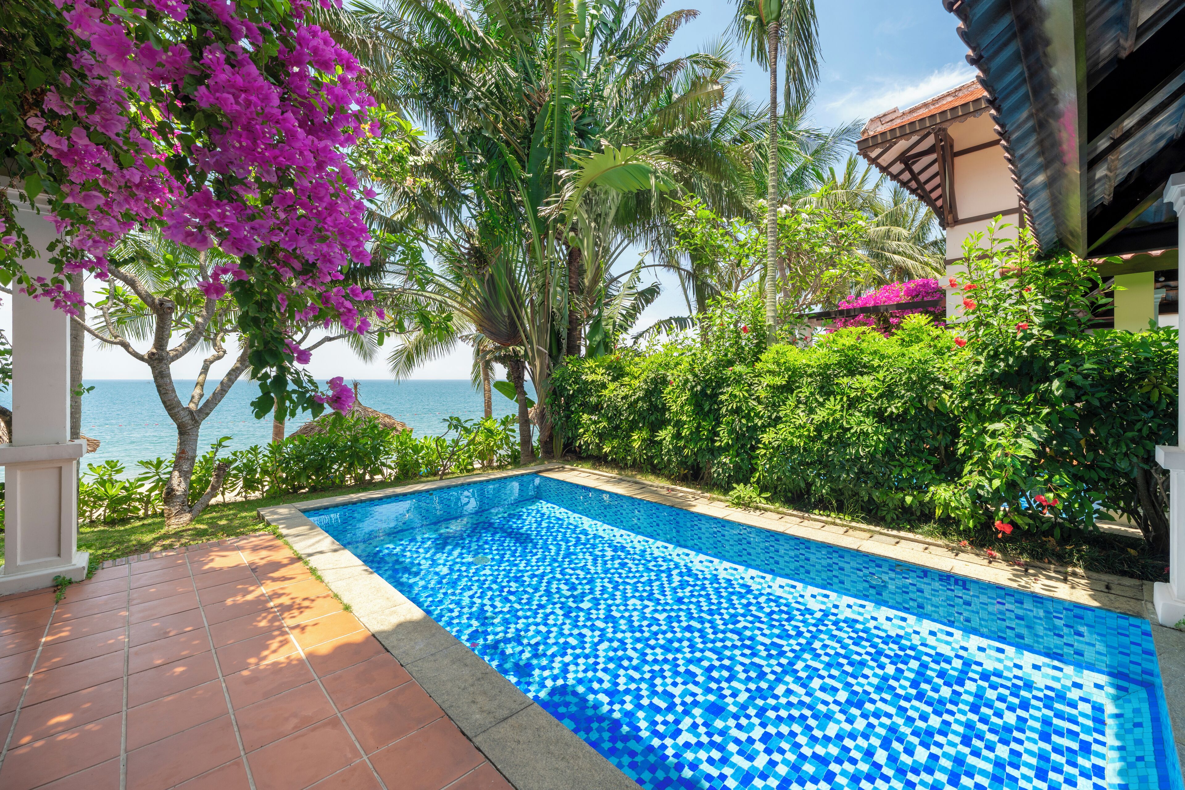 A swimming pool with a tiled edge, surrounded by lush greenery and a view of the sea.