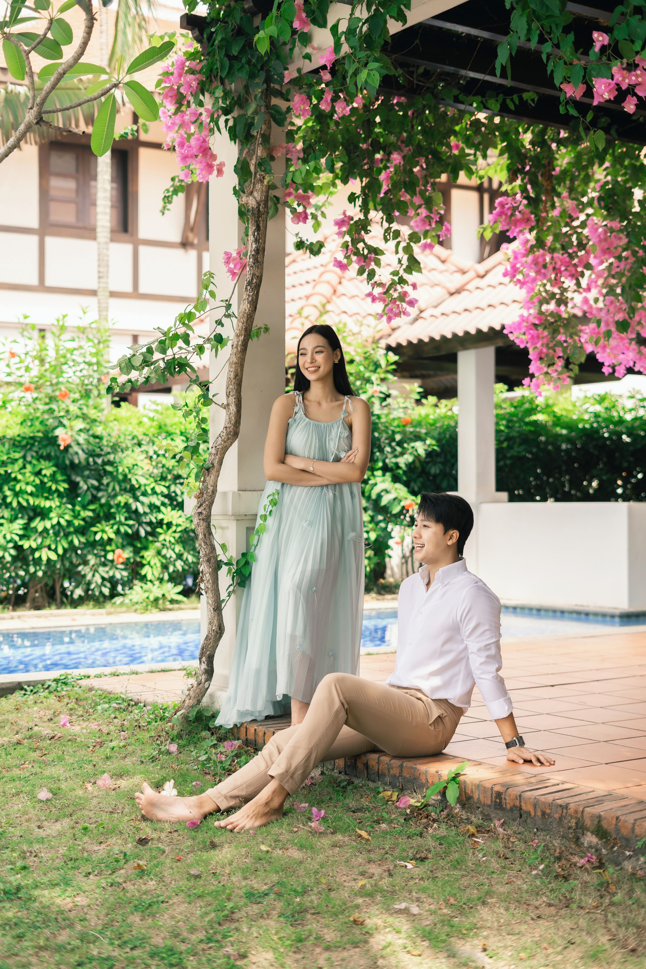Una pareja sentada junto a una piscina, con un jardín y un edificio al fondo.