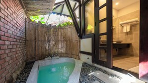 A spa area with a hot tub, a bamboo fence, and a view of a bathroom with a sink and towel rack. - Son Tra Resort (Da Nang)