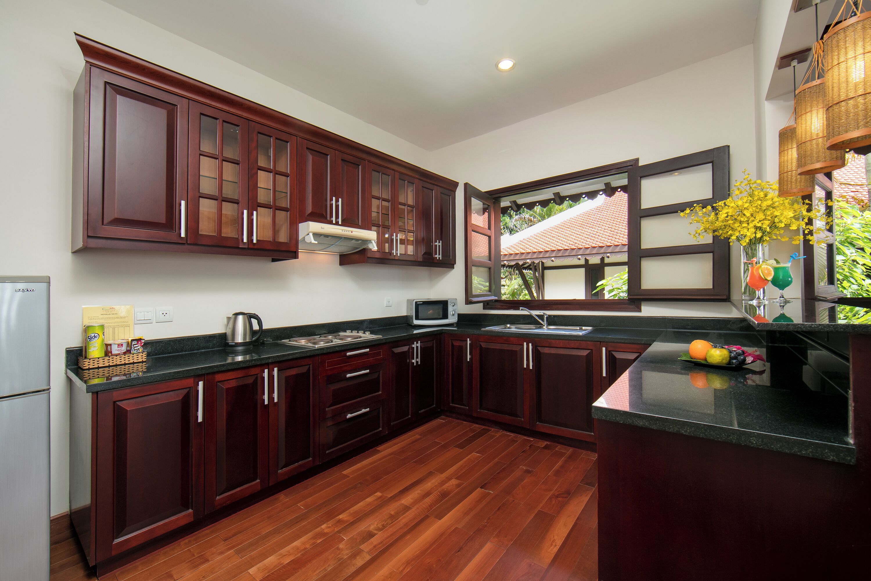 A kitchen with dark wooden cabinets, a microwave, and a window with a view of a house.