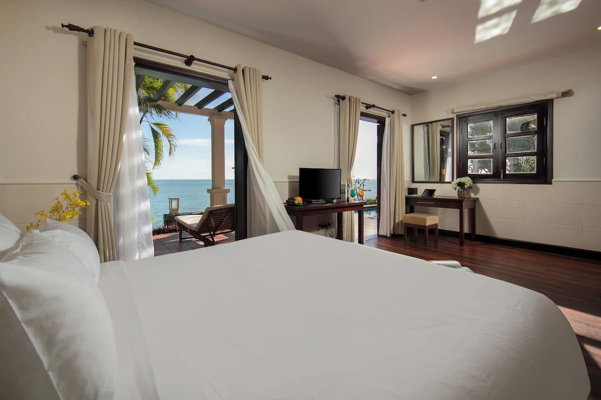 A bedroom with a large bed, a desk, a television, and a view of the ocean.