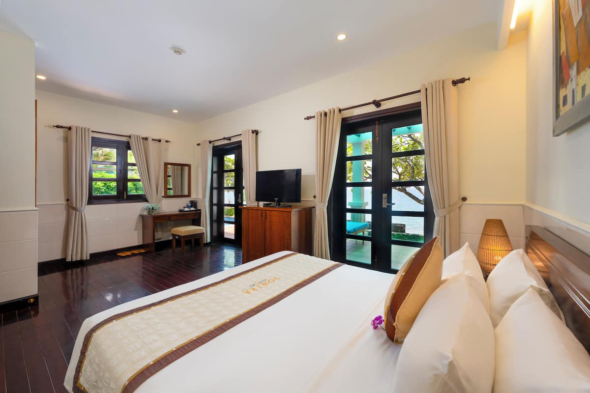 A hotel room with a large bed, a desk, a television, and a view of the outdoors.