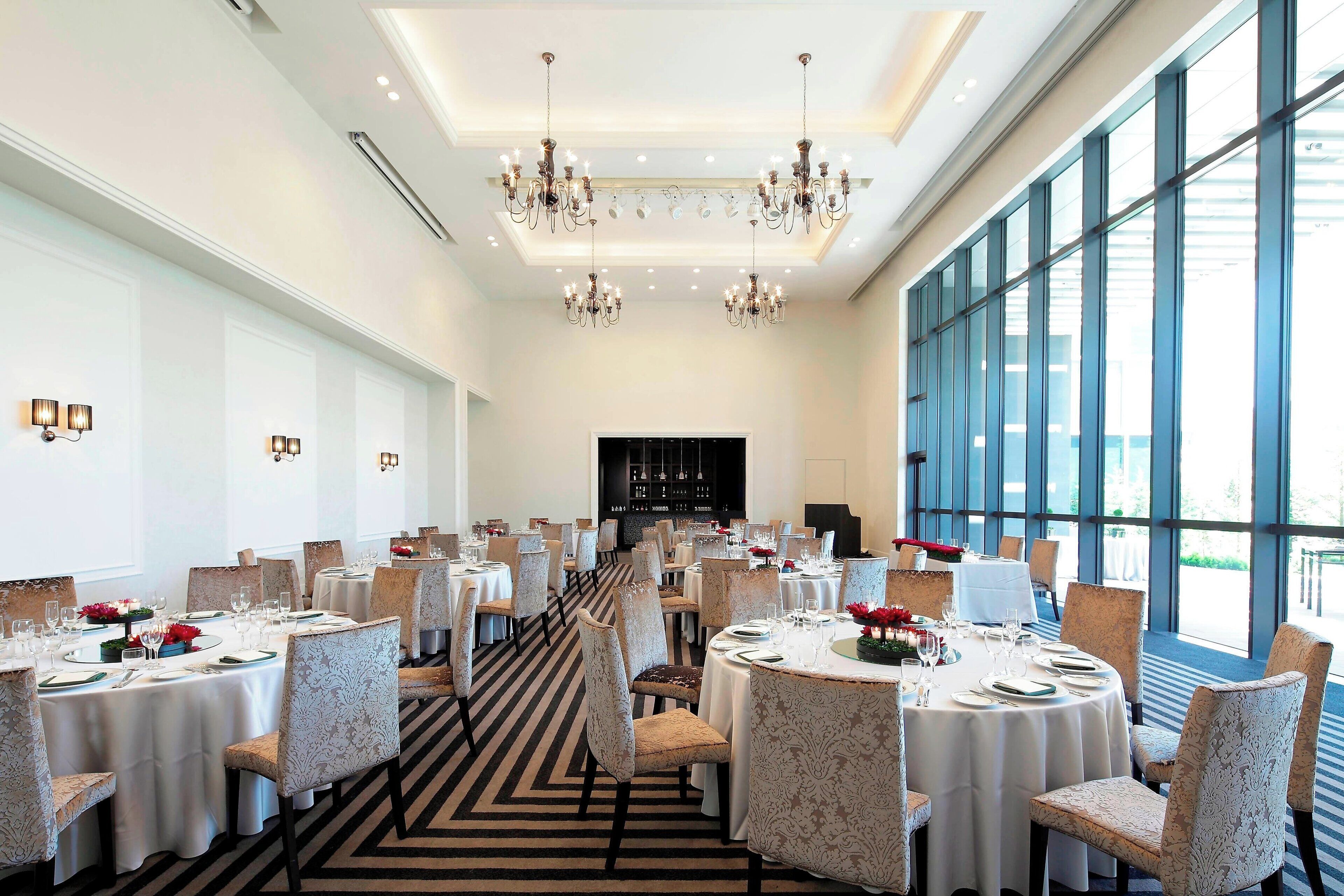 A spacious dining area with multiple round tables, elegant chandeliers, and large windows providing natural light.