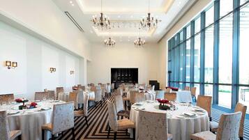 A spacious dining area with multiple round tables, elegant chandeliers, and large windows providing natural light.