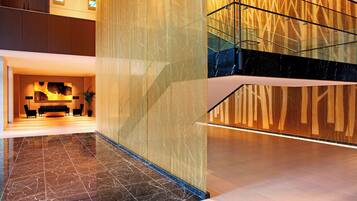 A modern lobby with a reception desk, a staircase, and a patterned wall.