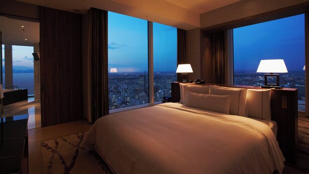 A spacious hotel room with a large bed, two bedside lamps, and a city view through floor-to-ceiling windows. - The Westin Sendai (Sendai)
