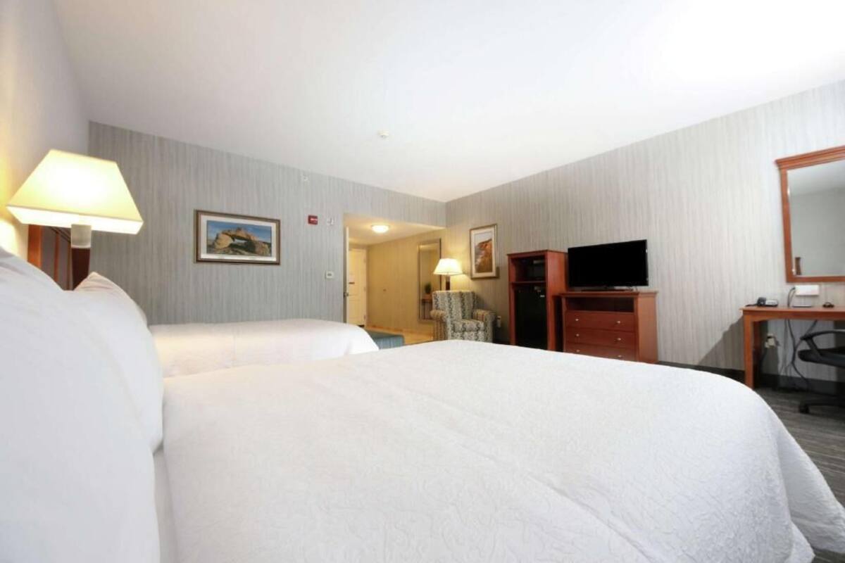 A hotel room with two beds, a desk with a chair, a television, and a door leading to another room.