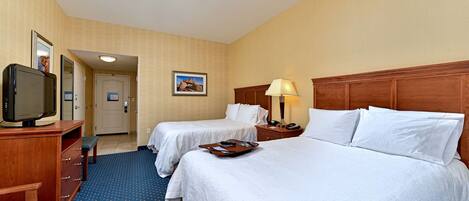 A hotel room with two beds, a TV, a desk, and a lamp.