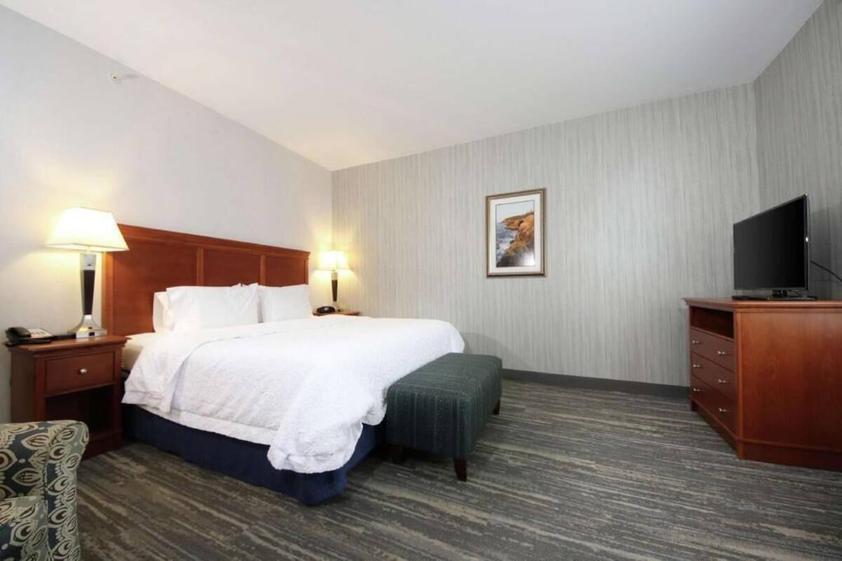 A hotel room with a bed, bedside lamps, a television, a desk, and a chair.