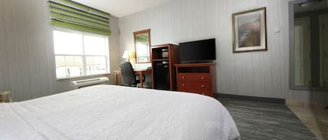 Une chambre d’hôtel avec un grand lit, un bureau avec une chaise, une télévision, un miroir et un tableau encadré au mur.