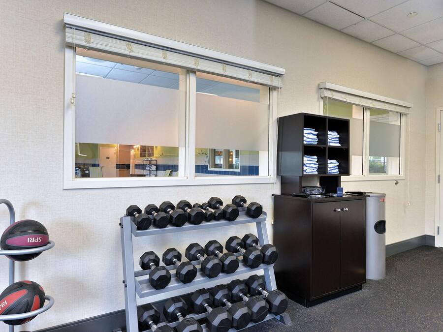 A gym with a rack of dumbbells, a cabinet with folded towels, and a window with a view of the interior.