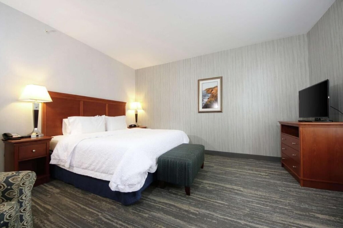 A hotel room with a bed, bedside lamps, a television, a desk, and a chair.