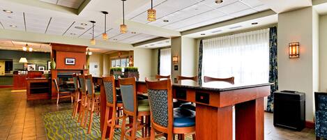 A hotel lobby with a bar area, wooden chairs, a patterned carpet, and pendant lighting.