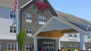 Un hôtel avec une façade en pierre, une enseigne bien visible indiquant « Hampton Inn », et un mât sur lequel flotte le drapeau américain.