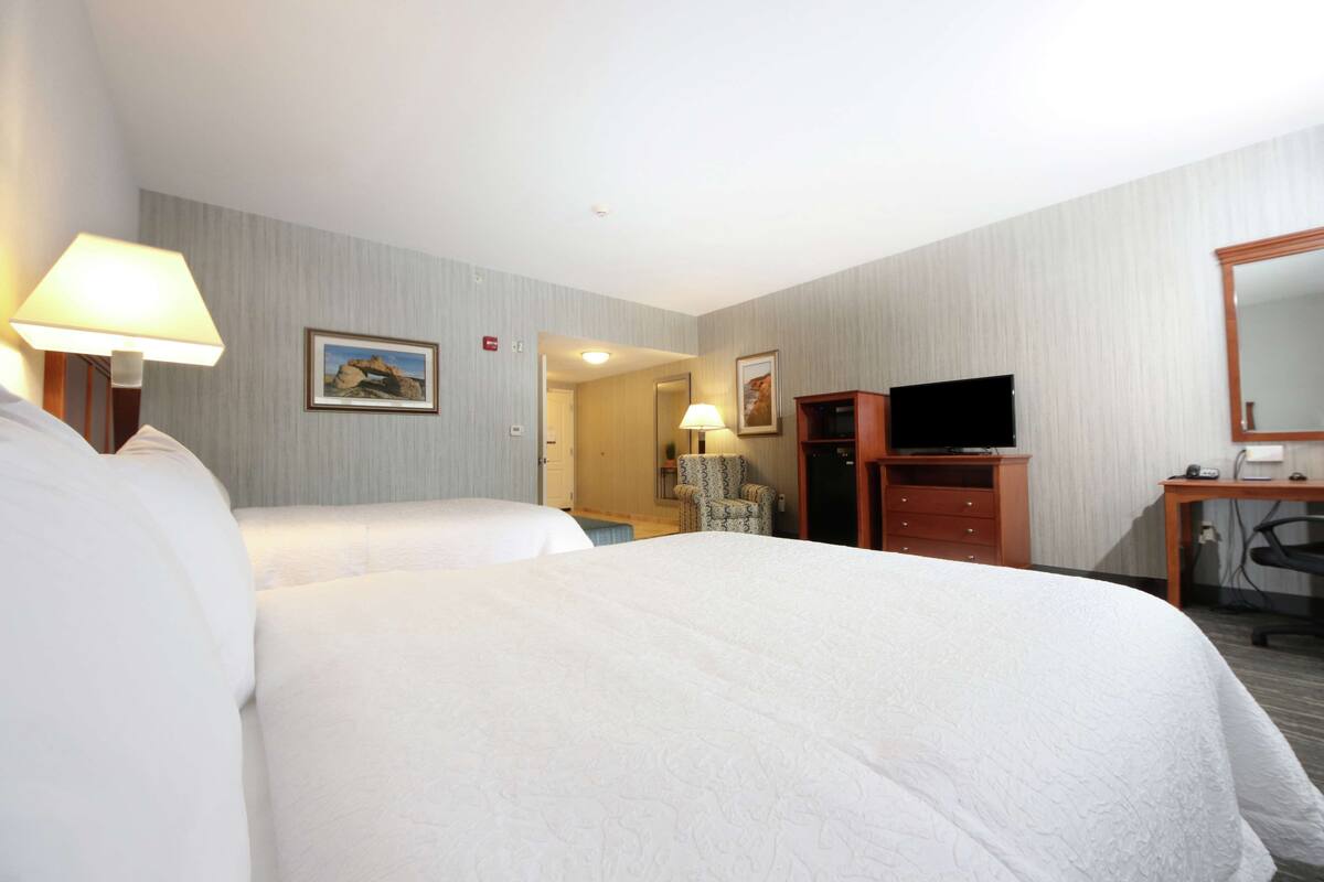 A hotel room with two beds, a desk with a computer, a TV, and a chair.