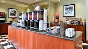 A breakfast bar with coffee makers, a stack of disposable plates, and a menu board.