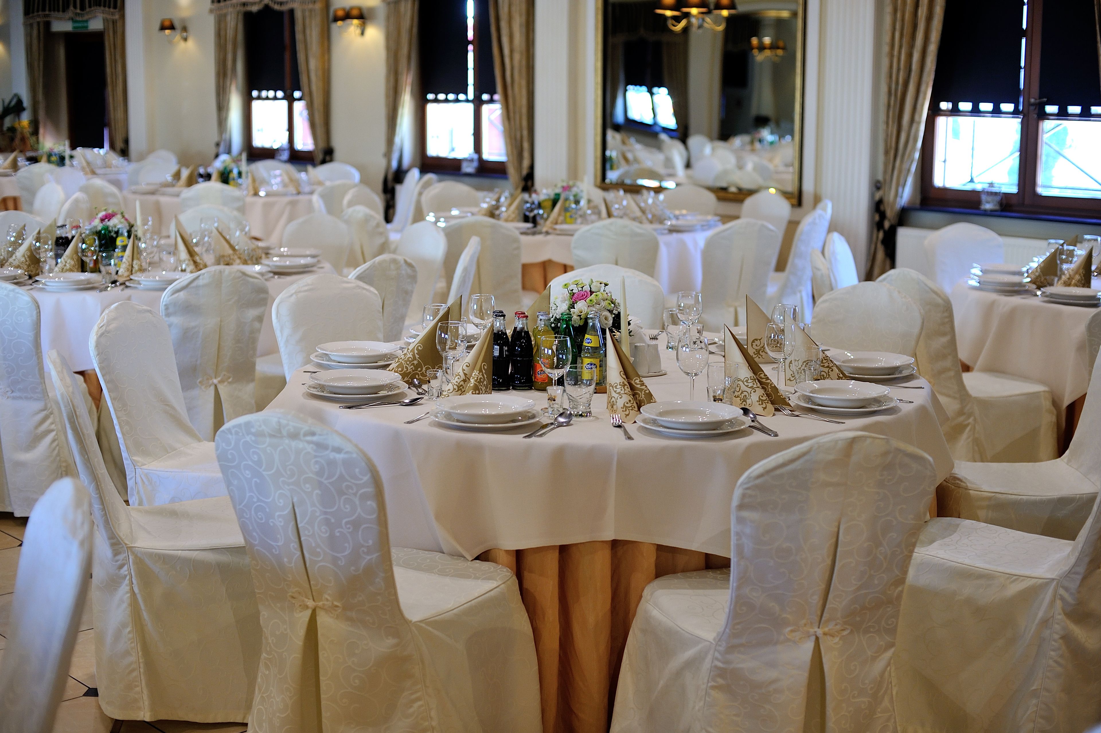 Un salón de banquetes con mesas redondas dispuestas para un evento formal, cada una con manteles blancos y centros de mesa dorados.