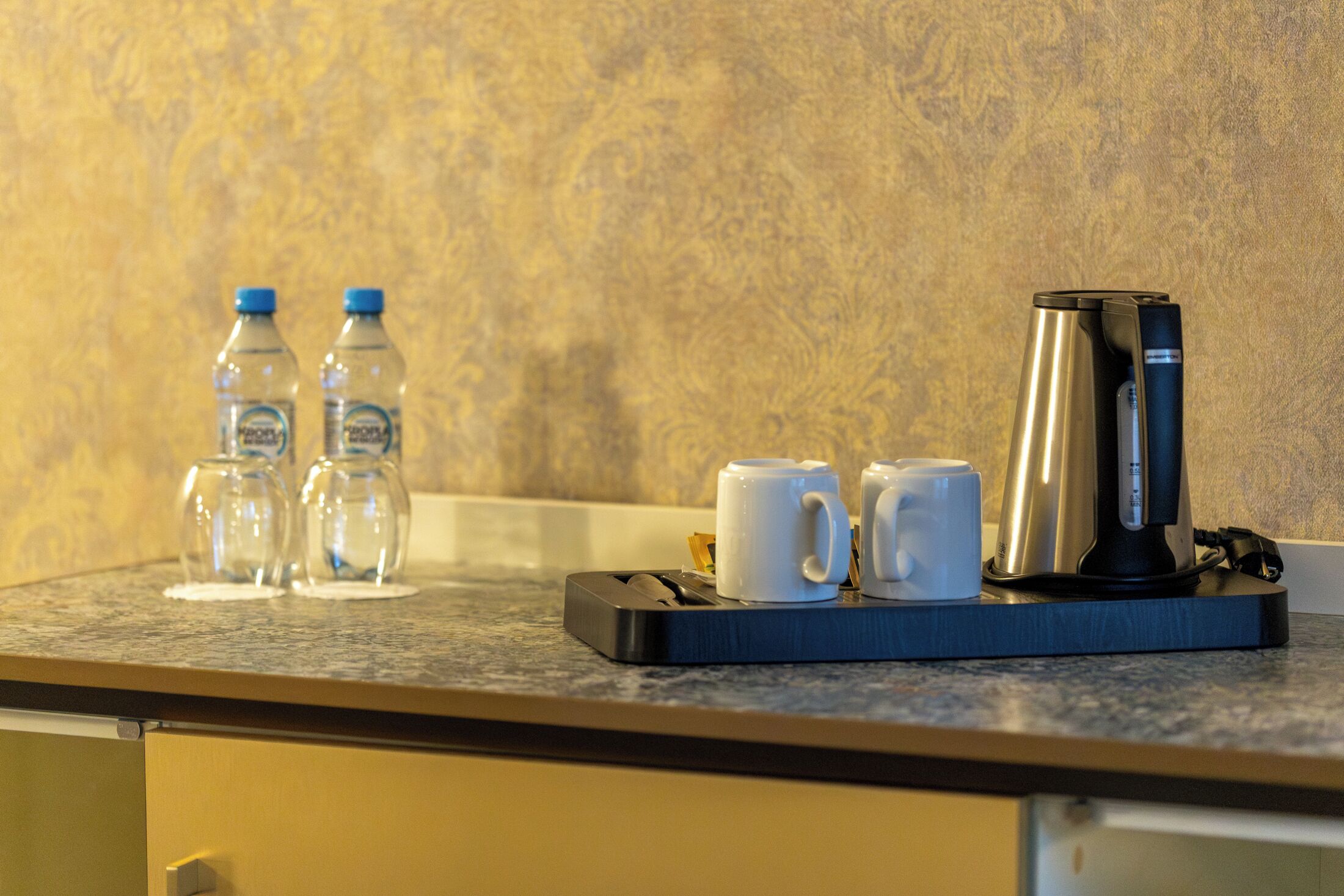 A kitchen counter with a coffee maker, two water bottles, and two white mugs.