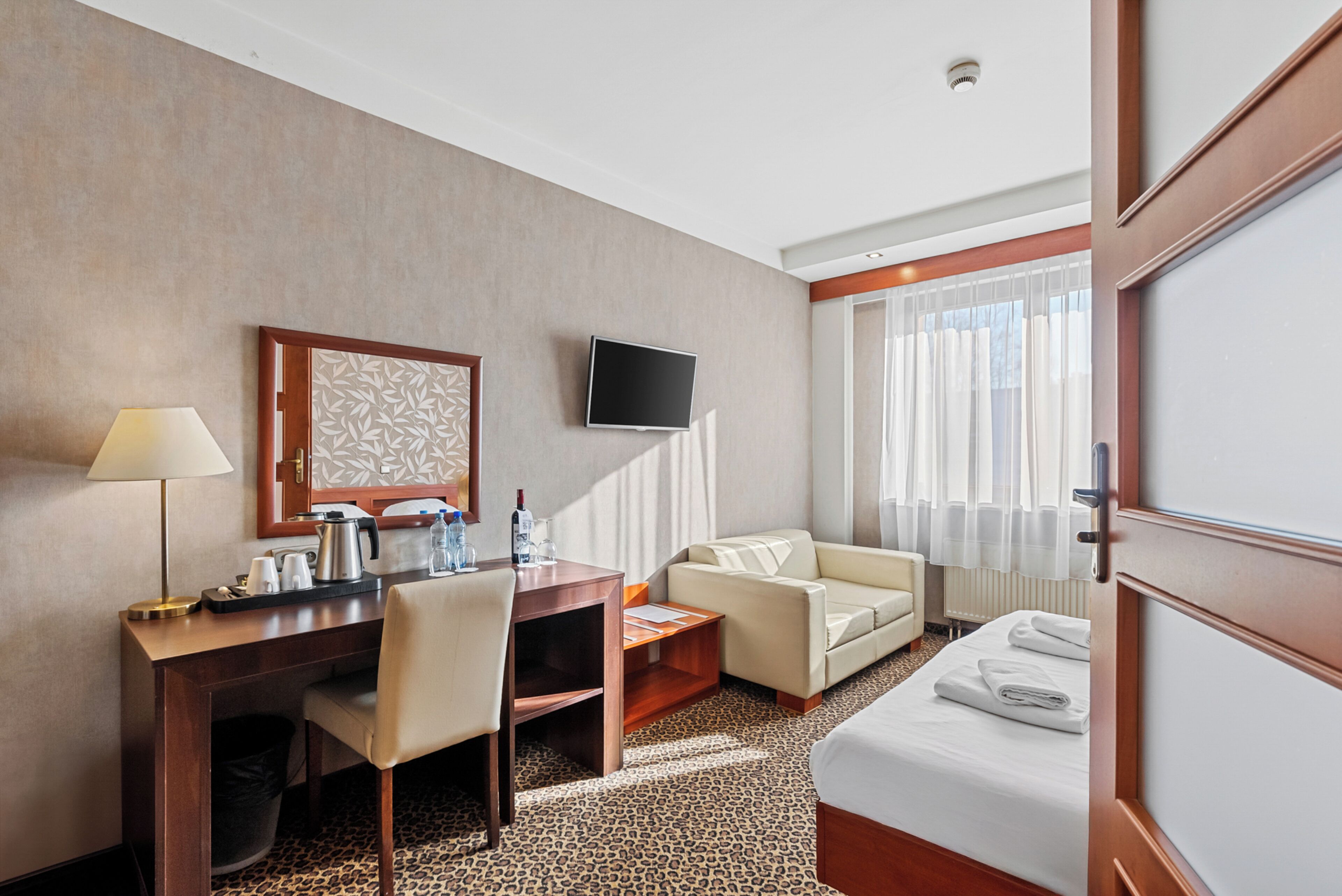 A hotel room with a desk, chair, sofa, bed, television, and a window with curtains.