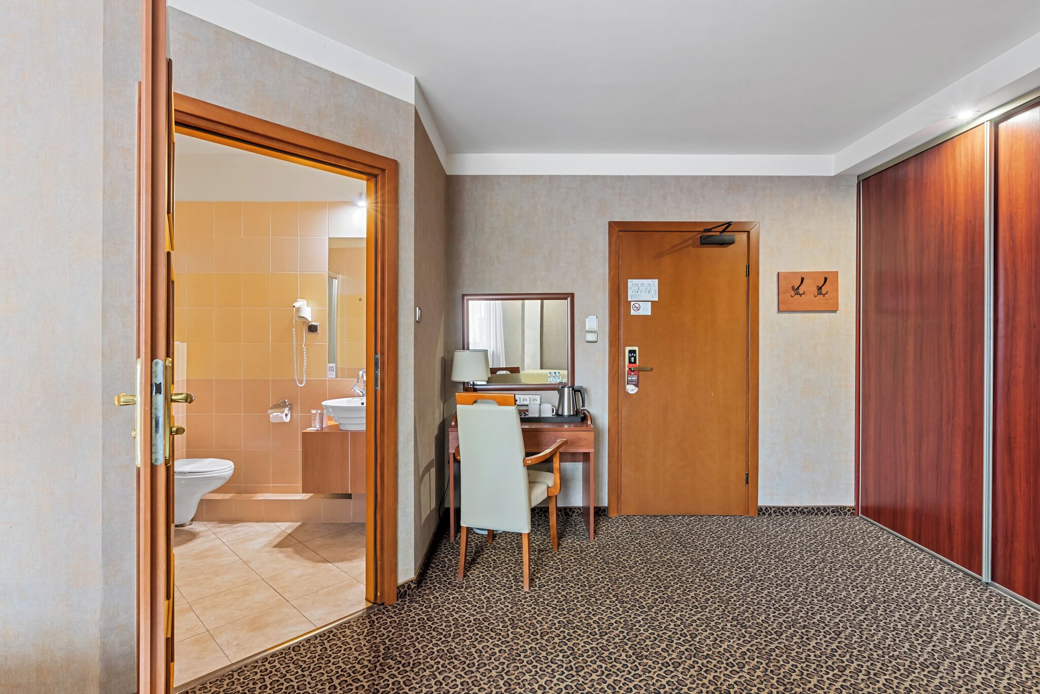 Une chambre d’hôtel équipée d’une douche, de toilettes, d’un bureau, d’une chaise et d’une porte donnant sur une autre chambre.